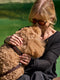 Woman cuddling a curly dog wearing a premium brown leather collar beside a lake.