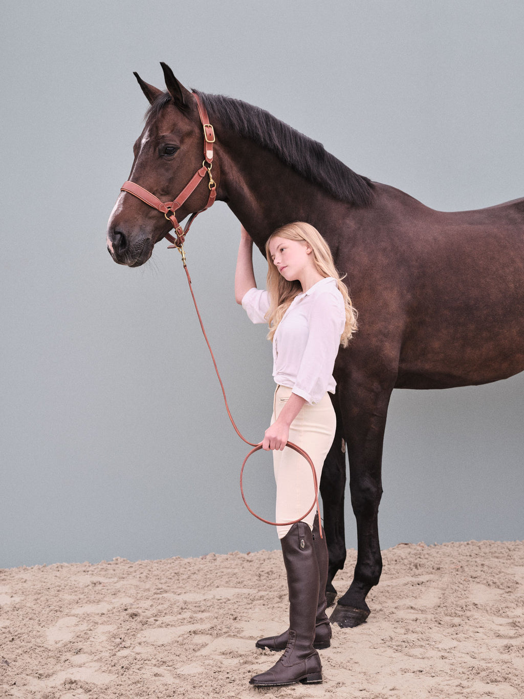 Rider standing beside a dark bay horse wearing a premium brown leather halter with matching lead rope.