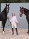 Equestrian rider standing between two horses wearing premium leather halters with matching lead ropes.