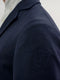 A close-up of a navy blue equestrian jacket shoulder featuring a tonal embroidered shield logo with the letter "V".