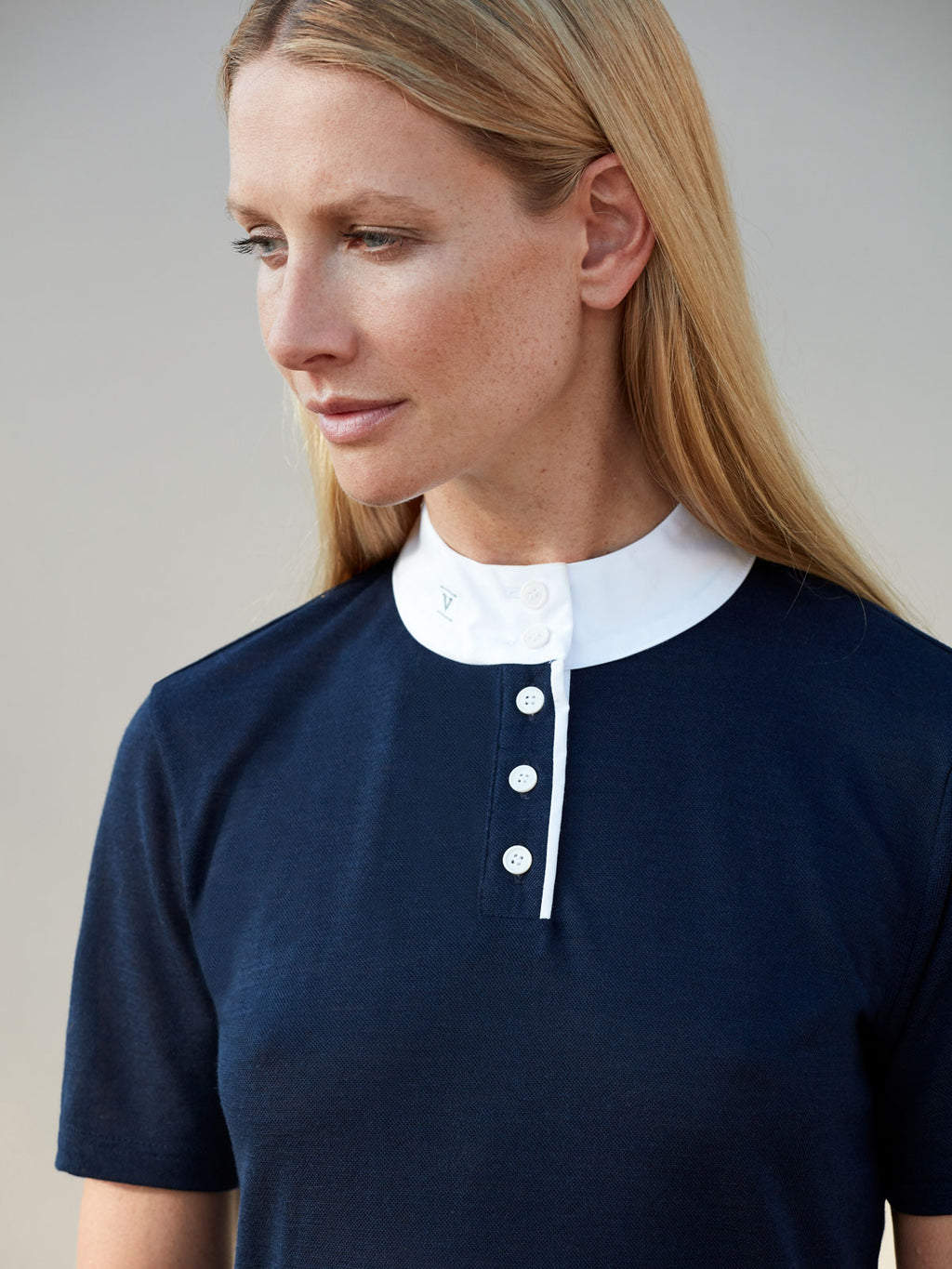 Blonde woman wearing a navy equestrian show shirt with a white high collar and buttons